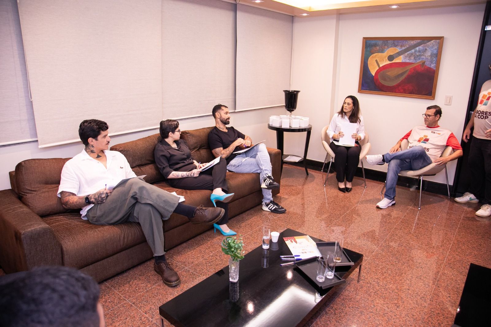 Cinco pessoas sentadas em um escritório, conversando. Um quadro está pendurado na parede.
