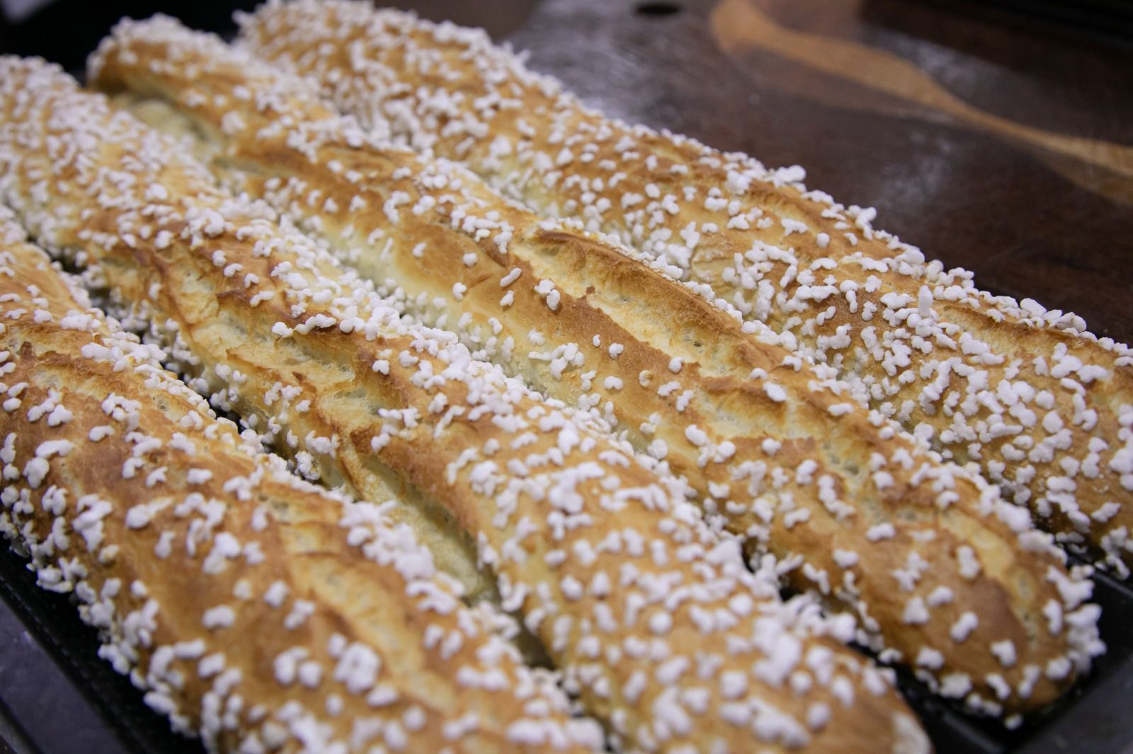 Quatro palitos de pão compridos, com crosta de açúcar, sobre uma superfície escura, dourada com cristais de açúcar branco.