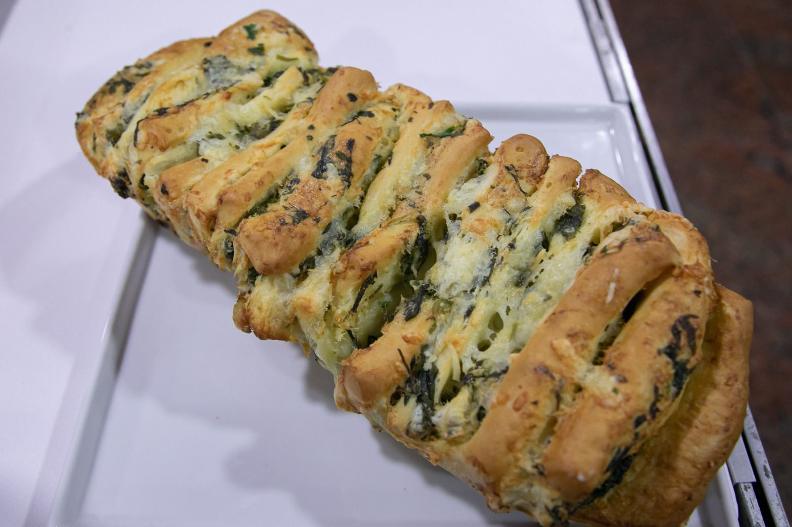 Pão trançado com ervas verdes em um prato retangular branco.