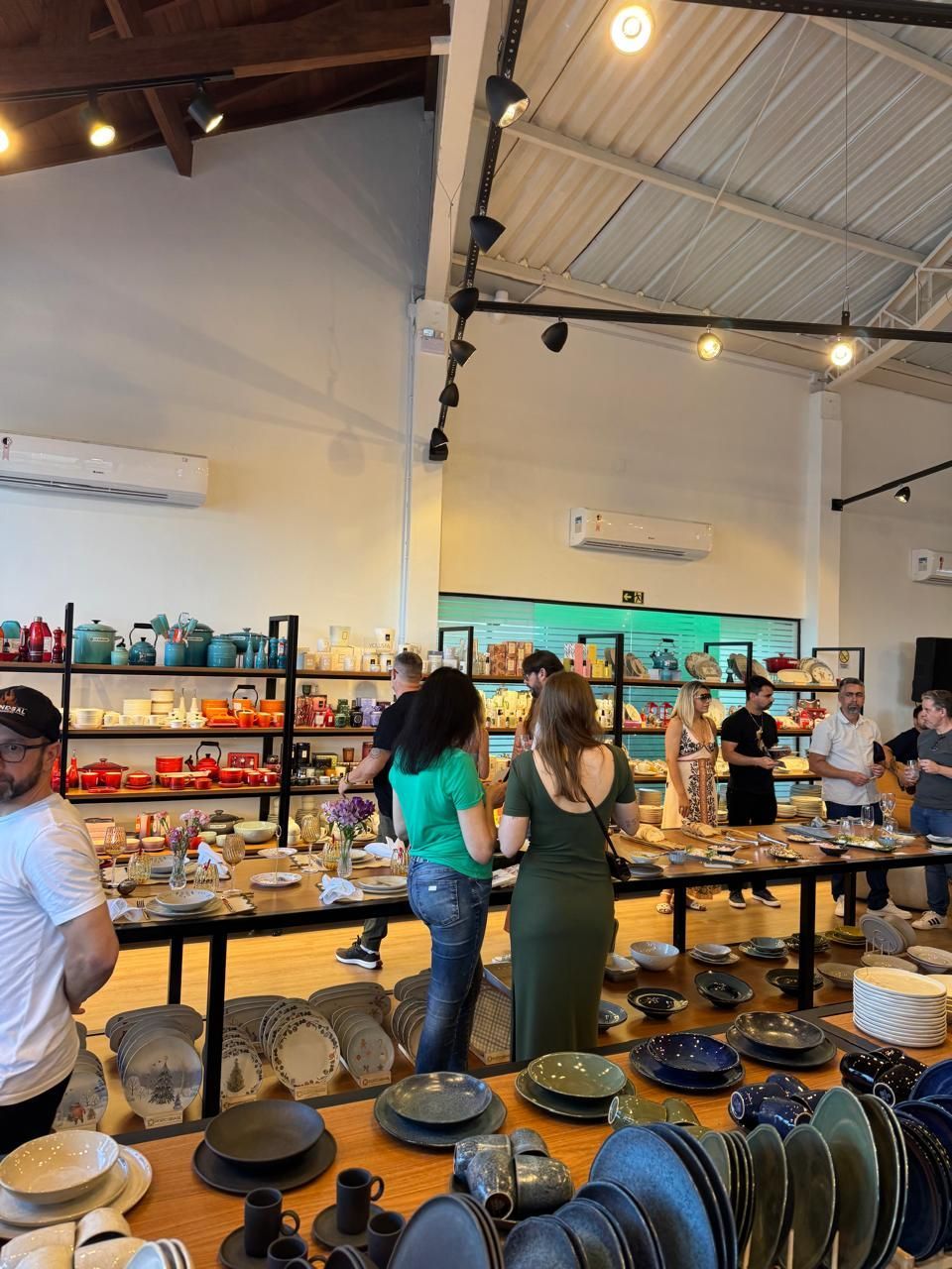 Pessoas observando utensílios de mesa em uma loja, com pratos, tigelas e outros itens de cozinha em exposição.