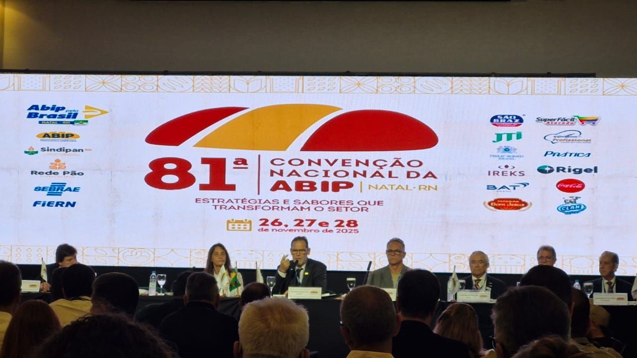 Conferência: Convenção da ABIP em Natal, Brasil. Palestrantes em uma mesa, telão com o logotipo ao fundo.