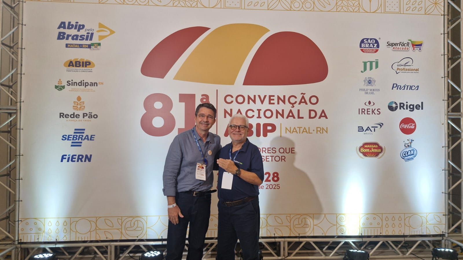 Dois homens posam em frente a uma faixa da 81ª Convenção Nacional em Natal, Brasil.