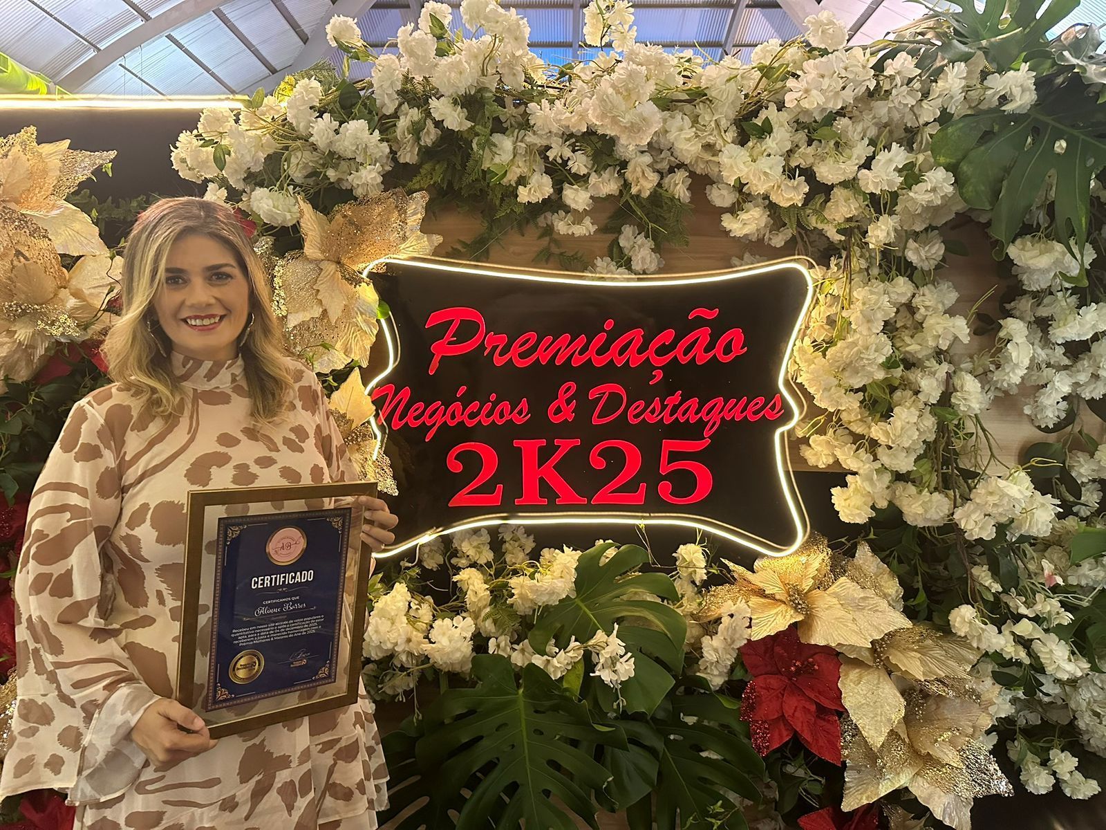 Woman holding award in front of floral display with text