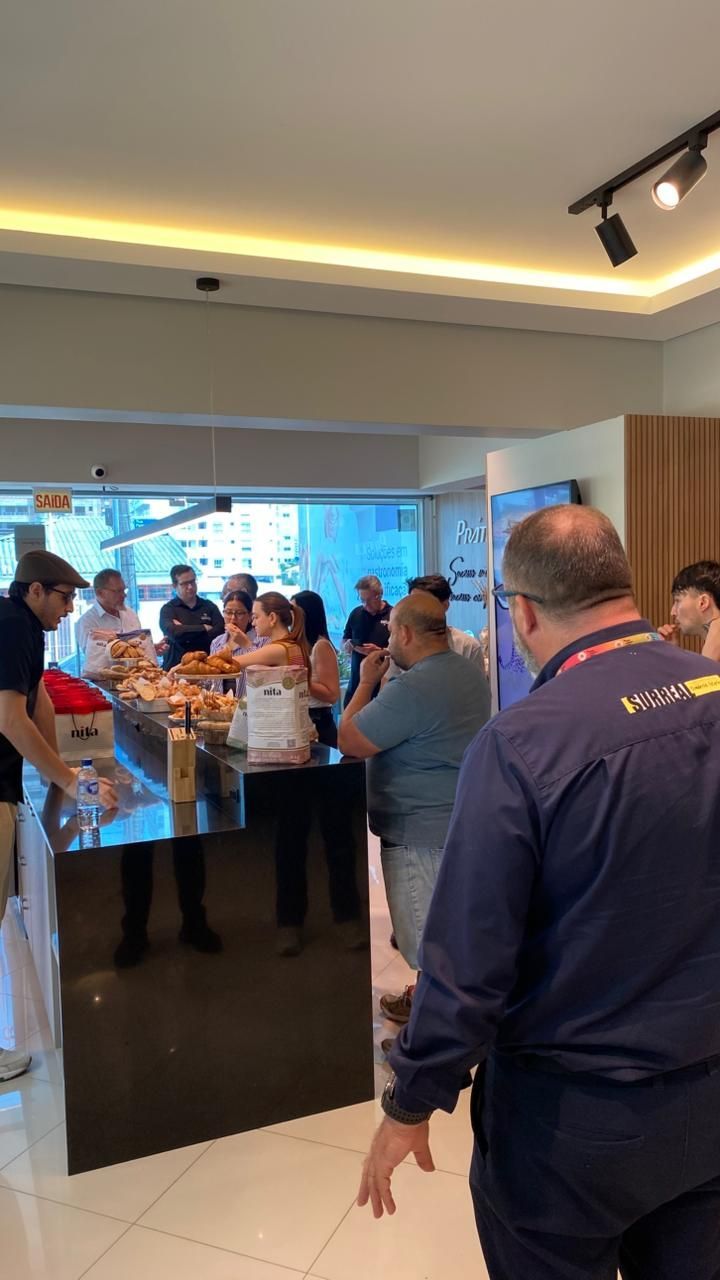 Pessoas reunidas em volta de um balcão com comida dentro de um ambiente bem iluminado.