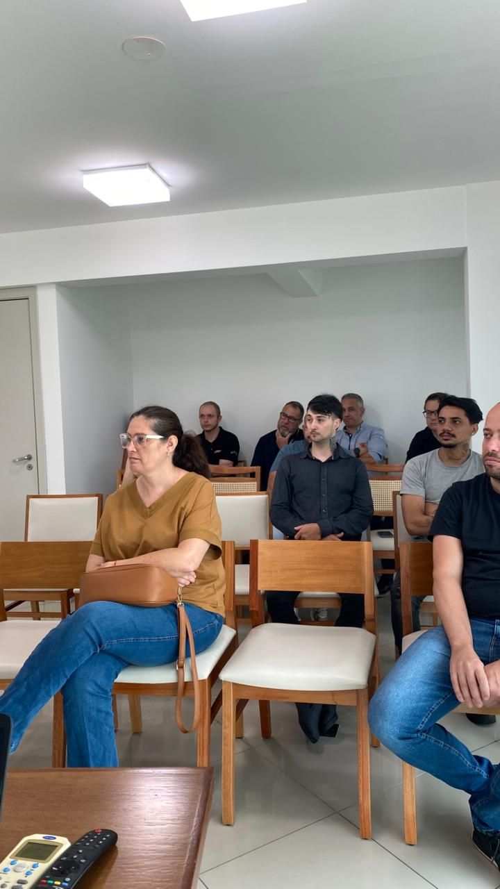 Pessoas sentadas em cadeiras, participando de uma reunião em uma sala bem iluminada.