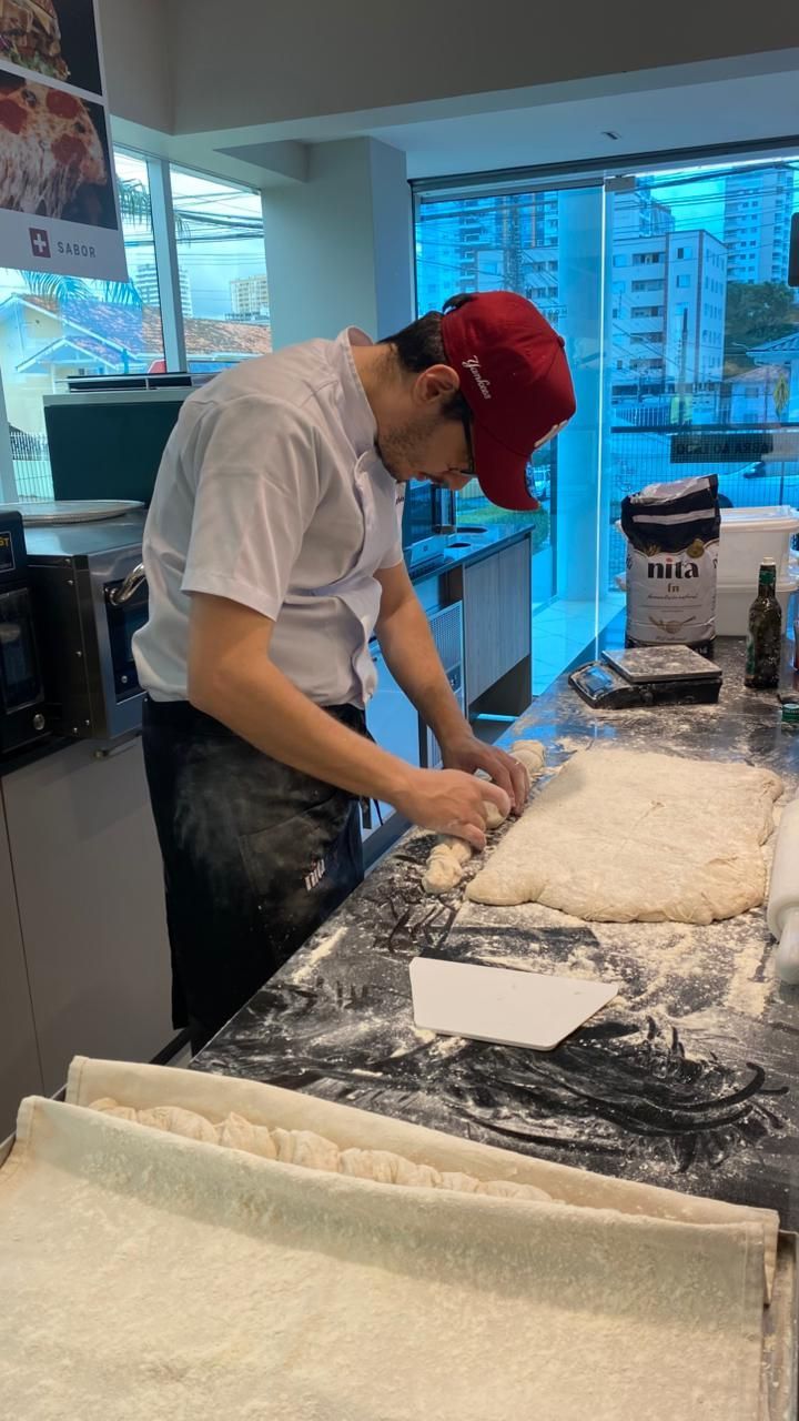 Chef de cozinha com boné vermelho trabalhando com massa em uma bancada preta.