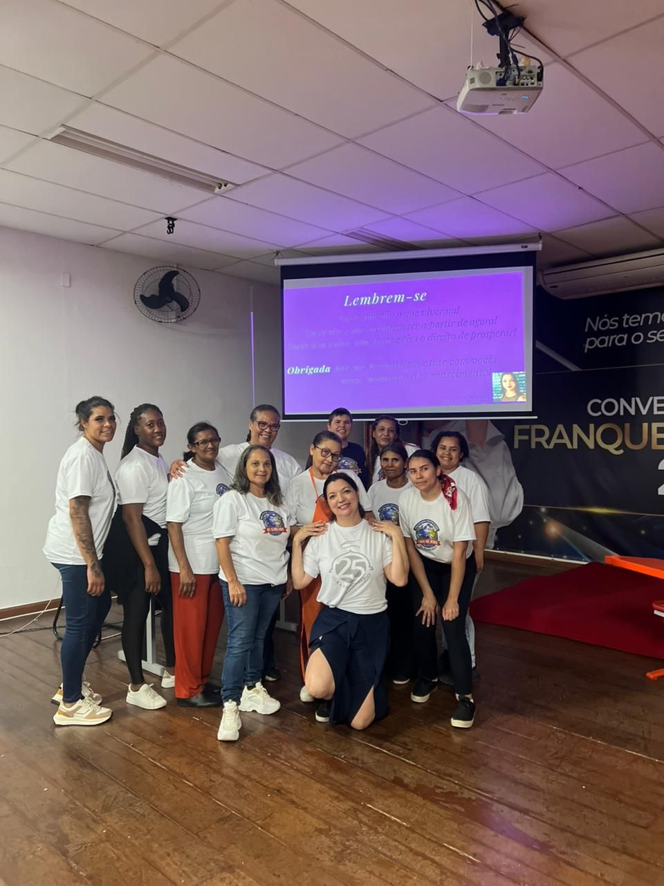 Um grupo de pessoas vestindo camisas brancas posa em frente a uma tela que exibe um texto.
