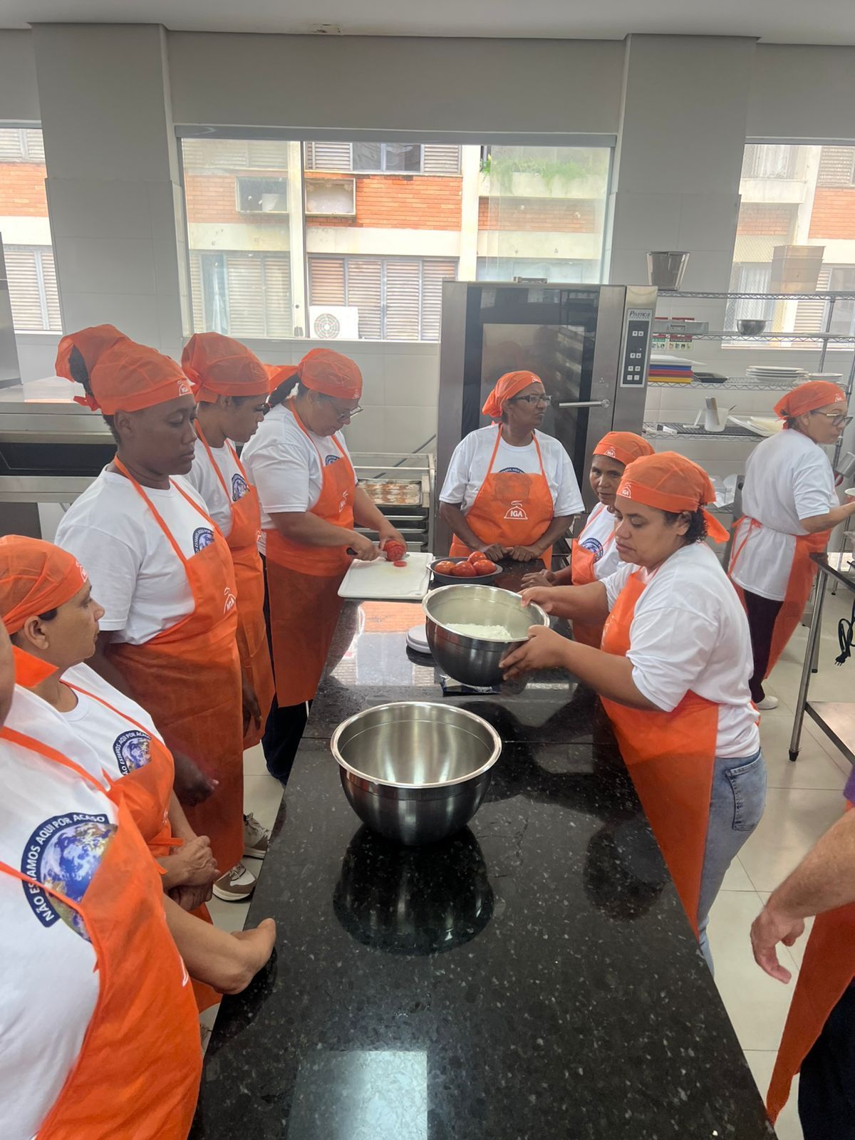 Grupo de pessoas com aventais e lenços na cabeça cor de laranja, preparando comida em uma cozinha.