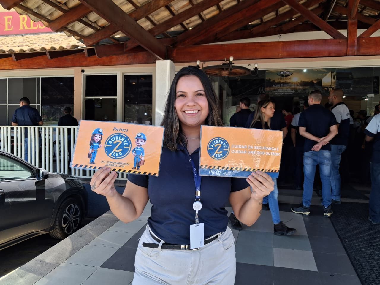 Mulher segurando duas placas laranjas, sorrindo em frente a um prédio.