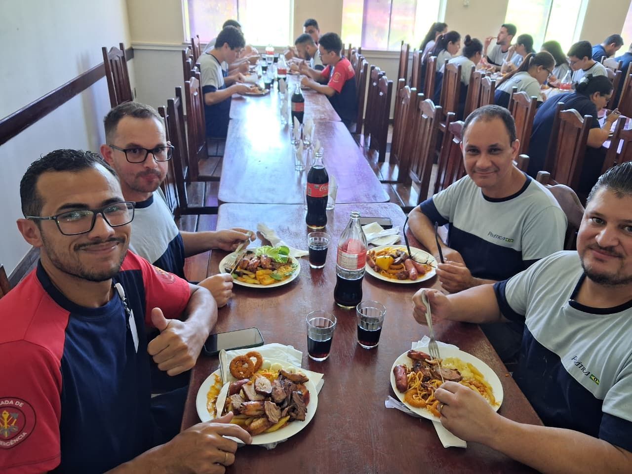 Grupo de pessoas em volta de uma mesa comprida, fazendo uma refeição
