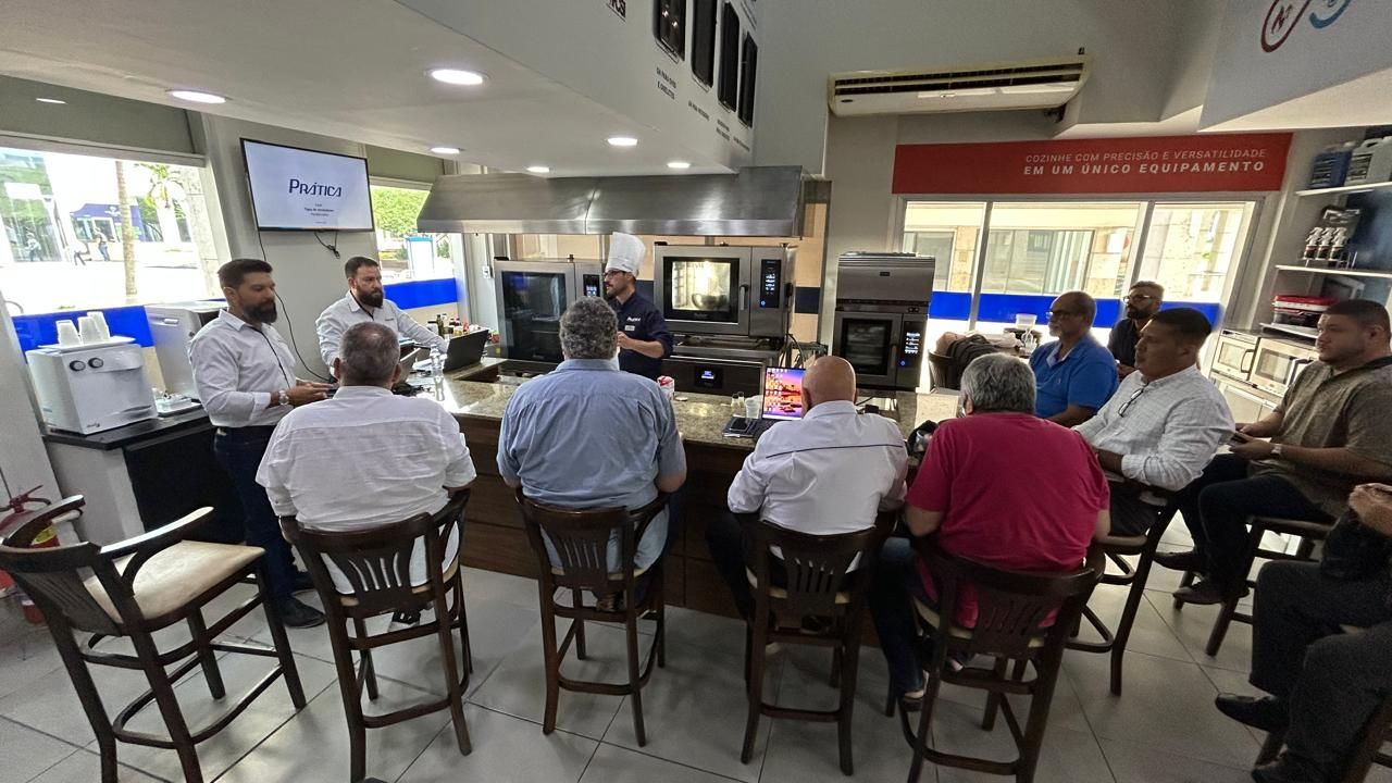 Pessoas em uma demonstração de eletrodomésticos de cozinha; um chef fala enquanto outros assistem.