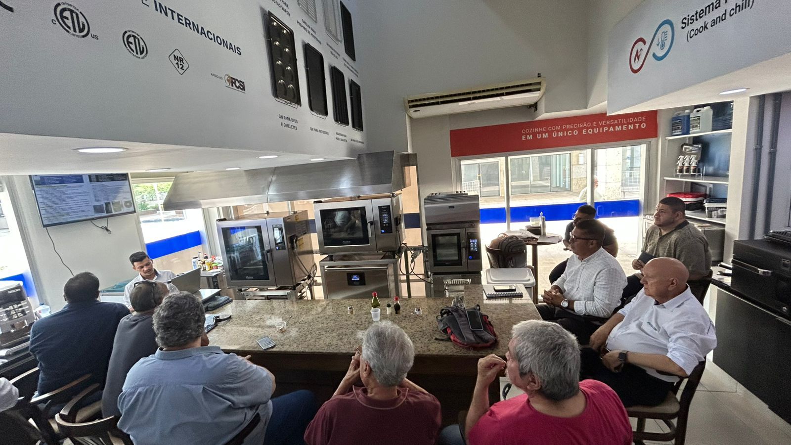 Grupo de pessoas assistindo a uma apresentação sobre eletrodomésticos de cozinha em um showroom.