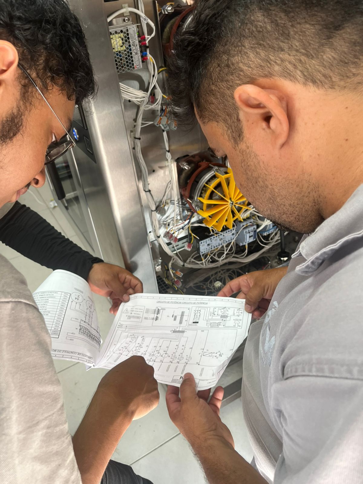 Dois técnicos examinando diagramas de fiação enquanto trabalham em máquinas.