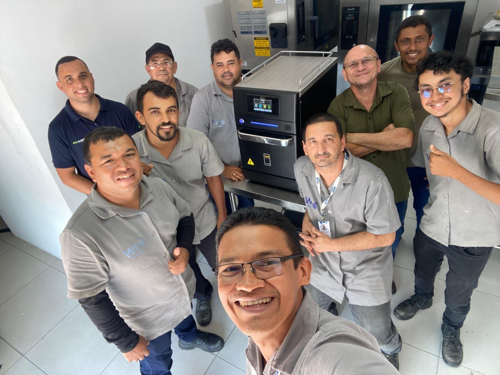 Grupo de técnicos sorrindo ao redor de uma máquina em um ambiente de laboratório.