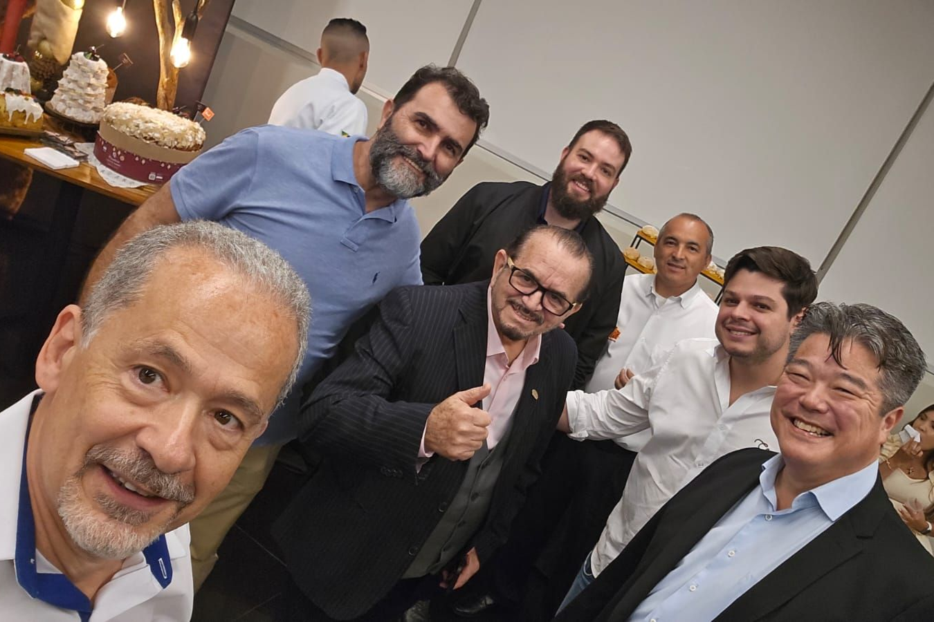 Grupo de homens sorridentes posando em ambiente interno. Alguns vestem ternos e camisas sociais.