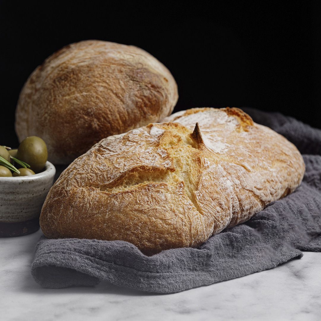 Um pedaço de pão está sobre uma toalha ao lado de uma tigela de azeitonas.