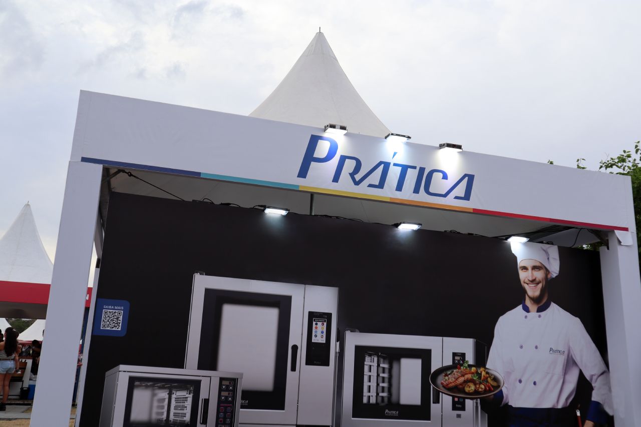Um homem com chapéu de chef segura um prato de comida sob uma placa que diz prática