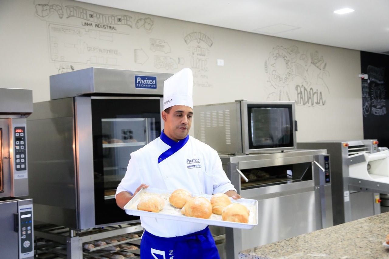 Um chef está segurando uma bandeja de pão em frente ao forno.