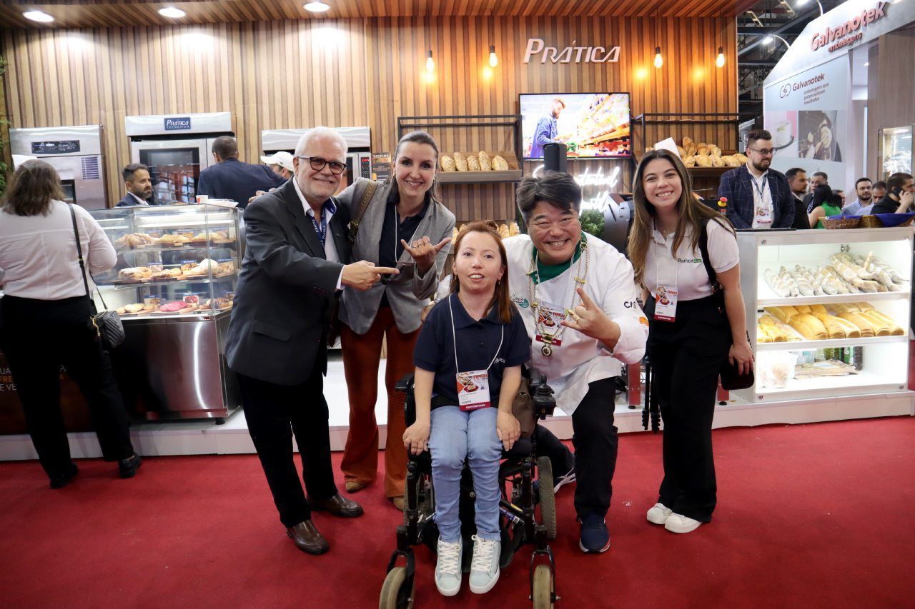 Um grupo de pessoas está posando para uma foto com uma garota em uma cadeira de rodas.