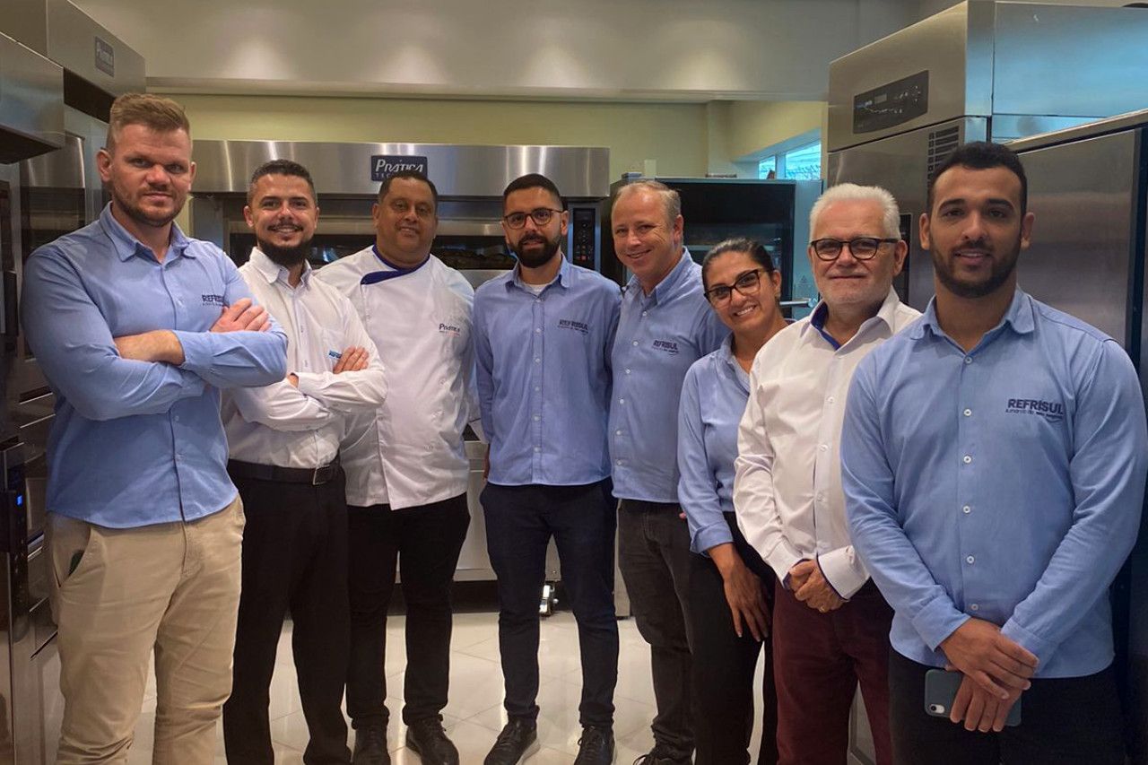 Um grupo de homens de camisa azul posa para uma foto em uma cozinha.