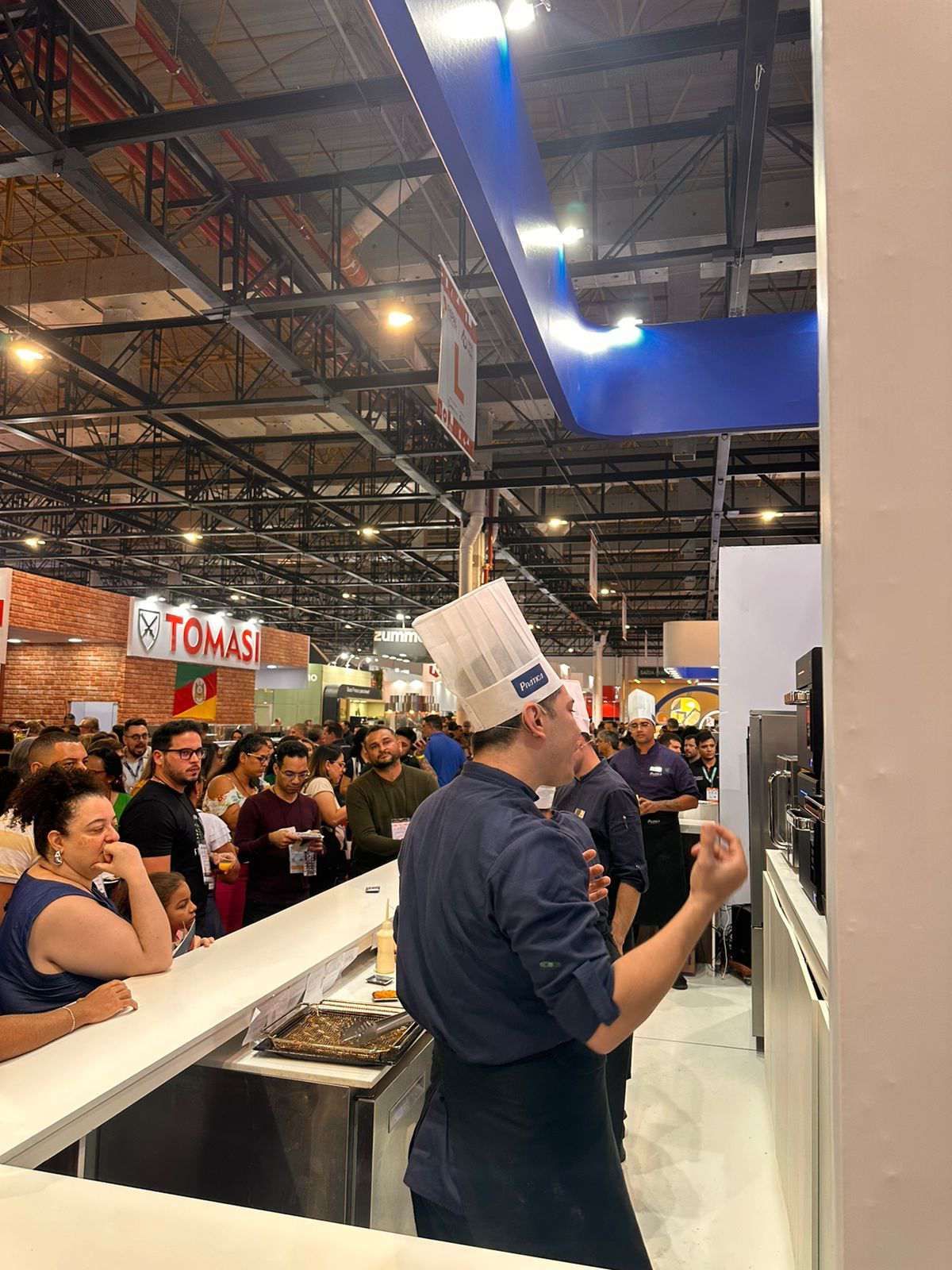 Um homem com chapéu de chef está parado na frente de uma multidão de pessoas.