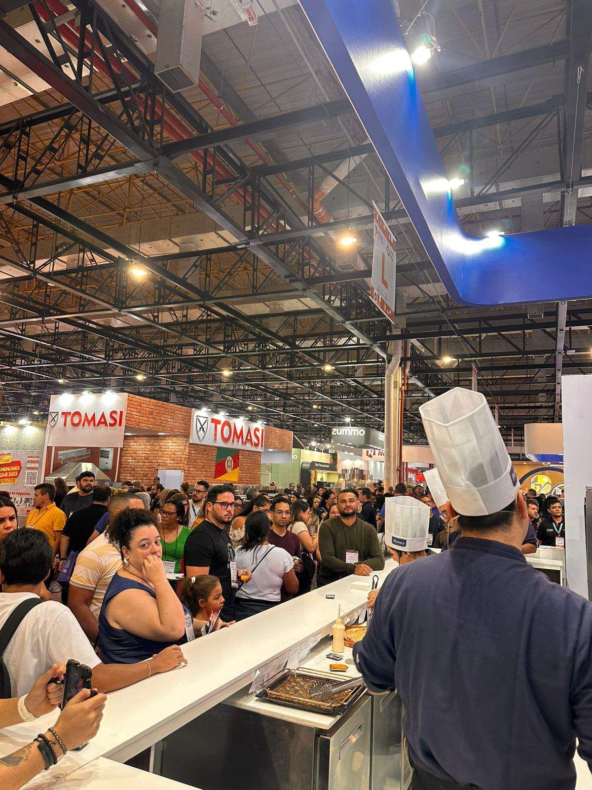 Um homem com chapéu de chef está parado na frente de uma multidão de pessoas.