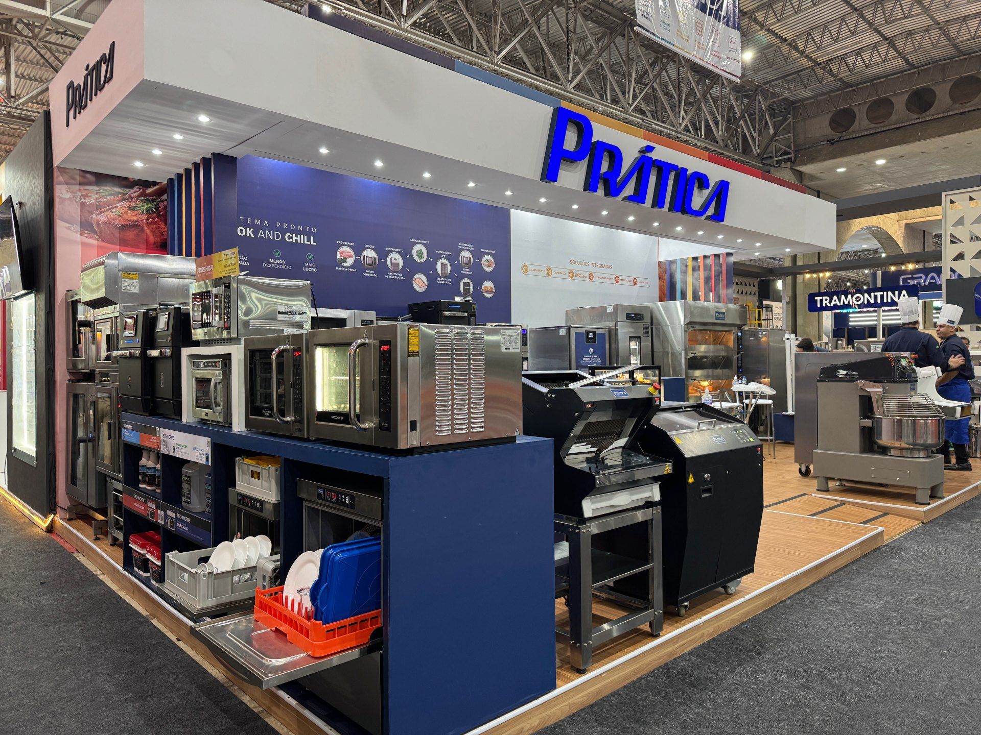 Estande da Prática em uma feira comercial, exibindo equipamentos para cozinhas industriais, com um esquema de cores azul e branco.
