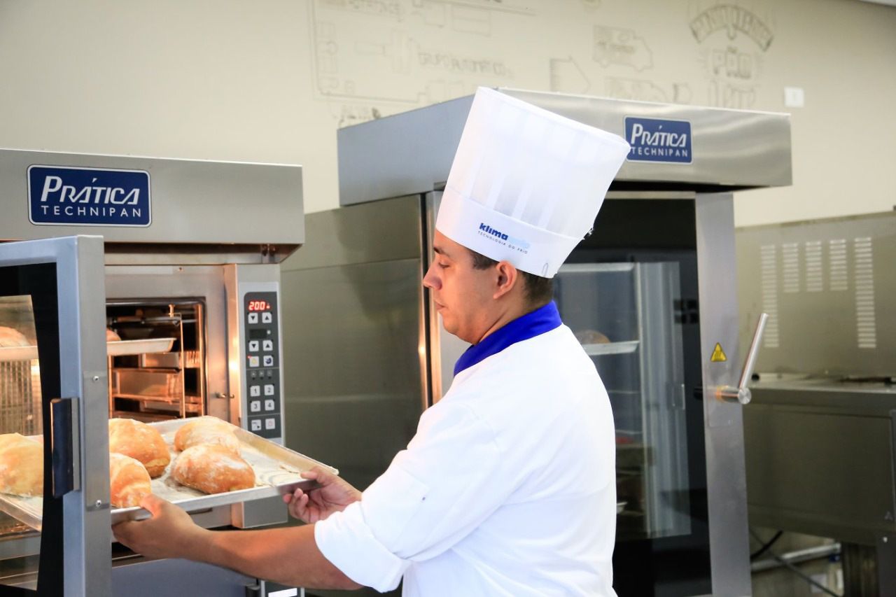 Um homem está tirando uma bandeja de pão do forno que diz pratica
