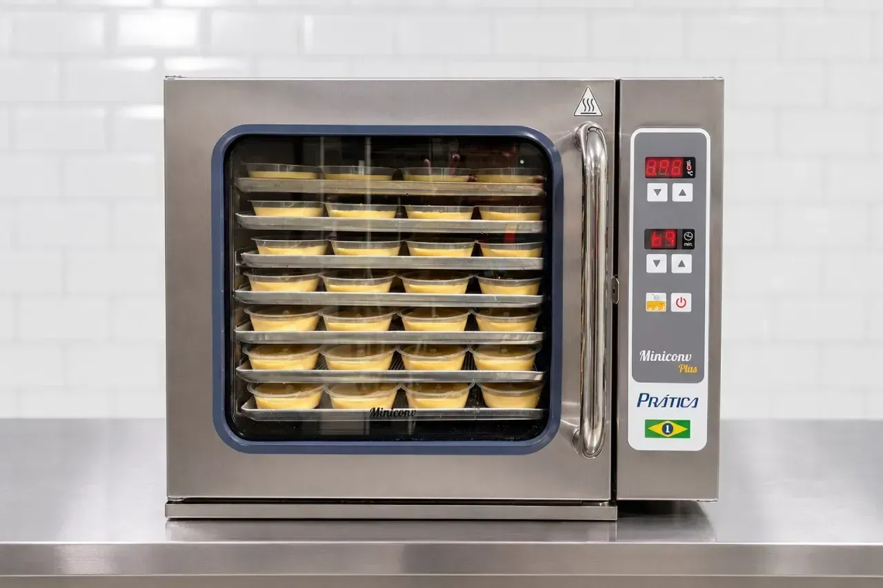 Forno comercial de aço inoxidável com bandejas de produtos assados ​​em seu interior, sobre uma bancada de cozinha.