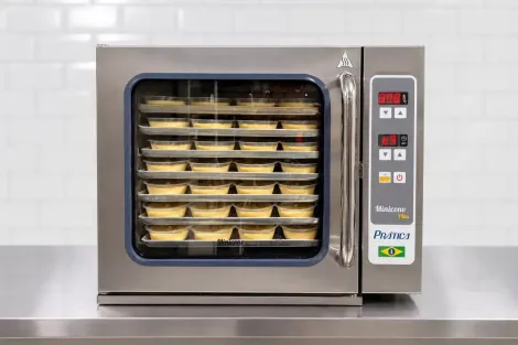 Forno comercial de aço inoxidável com bandejas de produtos assados ​​em seu interior, sobre uma bancada de cozinha.