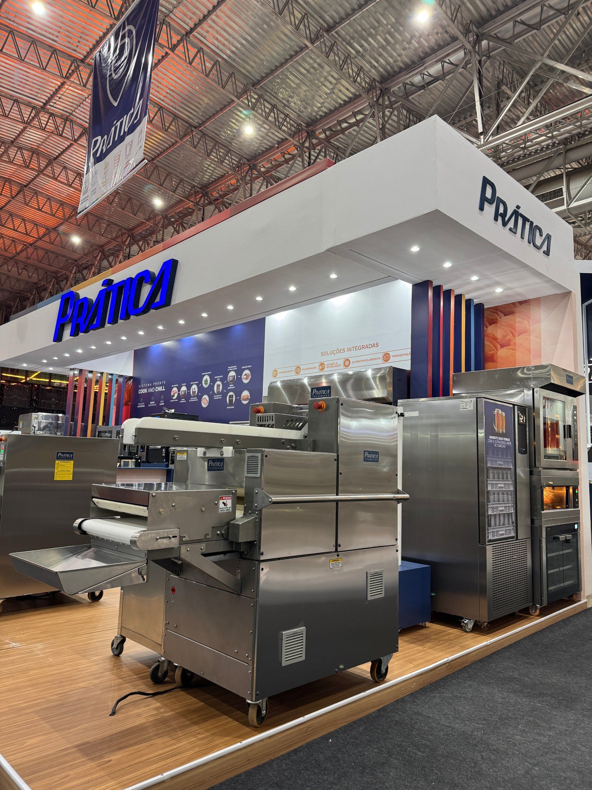 Um estande em uma feira comercial exibe equipamentos industriais para panificação sob a placa 