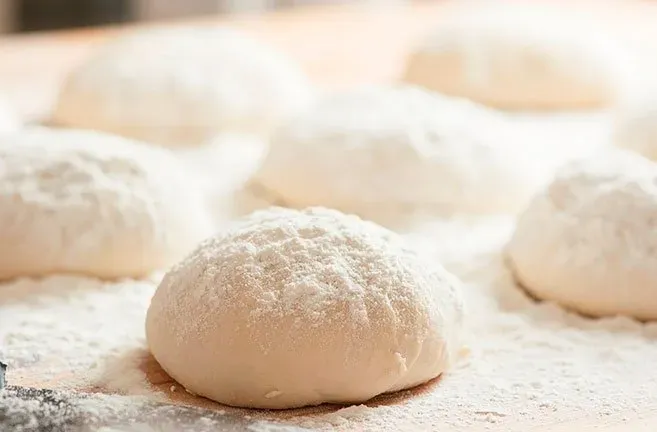 Um monte de bolas de massa em cima de uma mesa coberta de farinha.