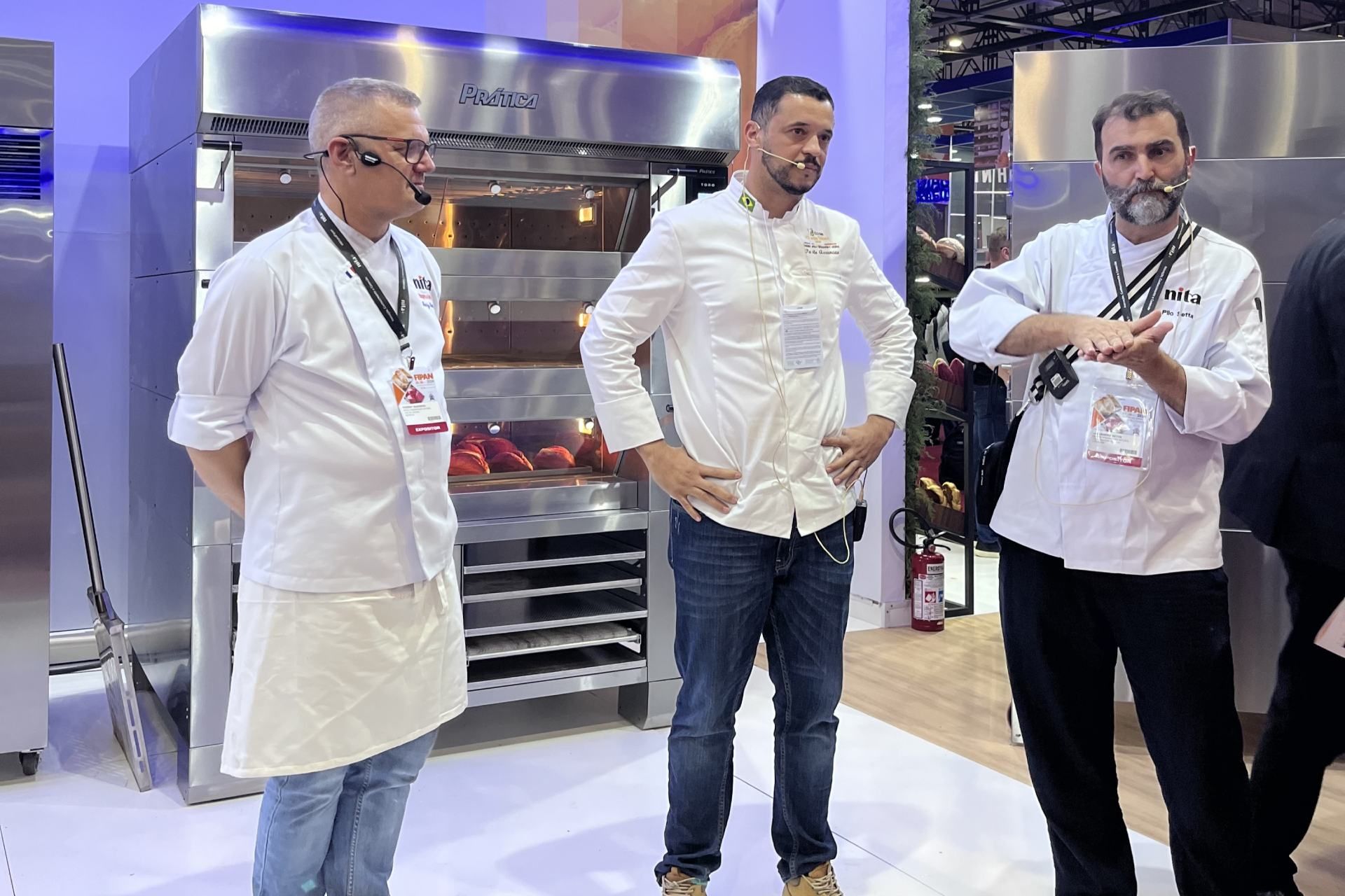 Três homens estão diante de um forno de aço inoxidável.