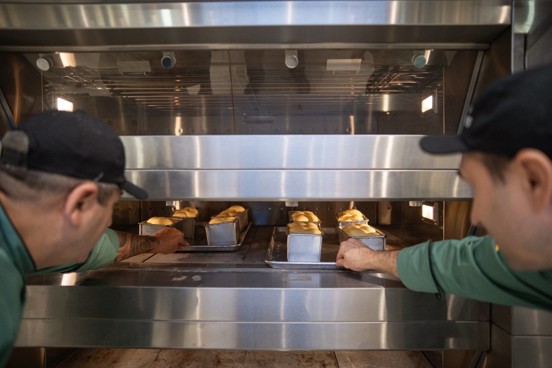 Dois homens estão olhando para um forno de aço inoxidável cheio de pão.