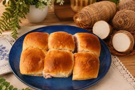 Seis pãezinhos dourados de inhame em um prato azul com enfeites de vime e folhagens ao fundo.