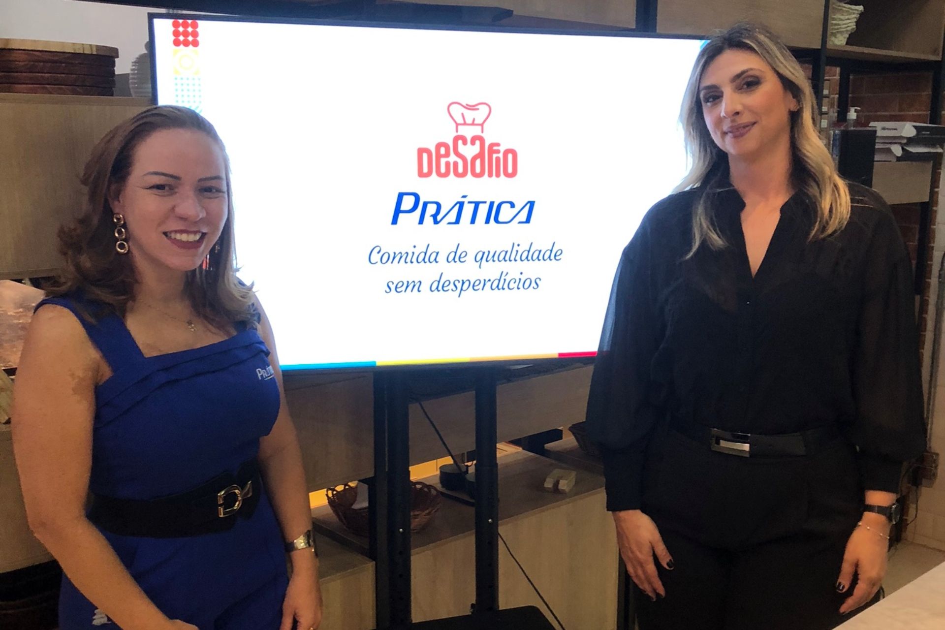 Duas mulheres estão em pé ao lado de uma tela com os dizeres
