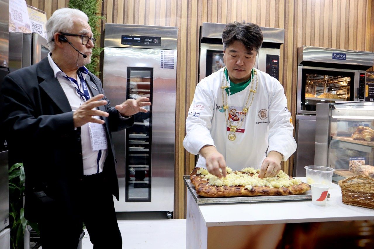 Um homem de terno está ao lado de um chef cortando uma pizza.