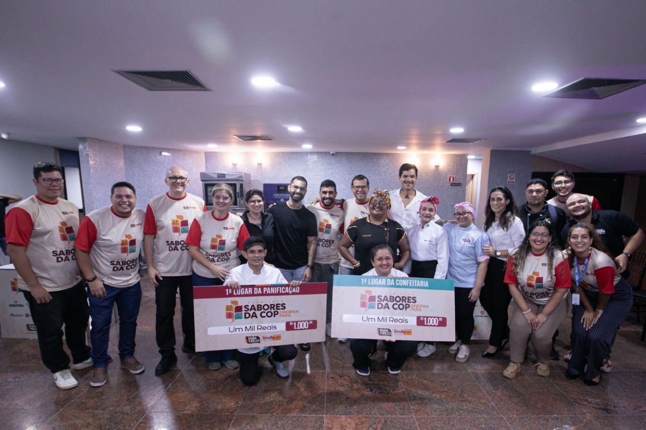 Grupo de pessoas sorrindo enquanto seguram cheques de doação. Evento em ambiente fechado.