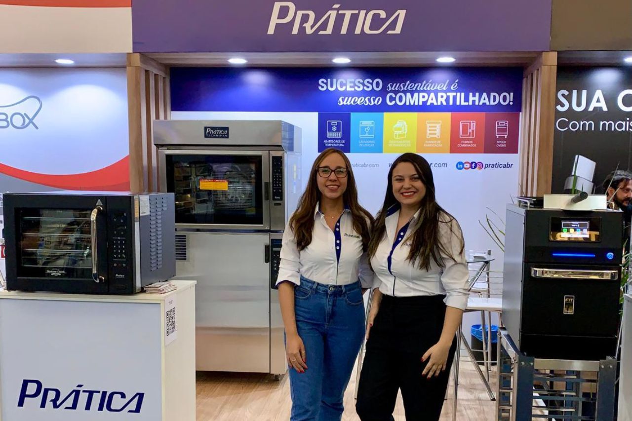 Duas mulheres de camisa branca estão em uma barraca 