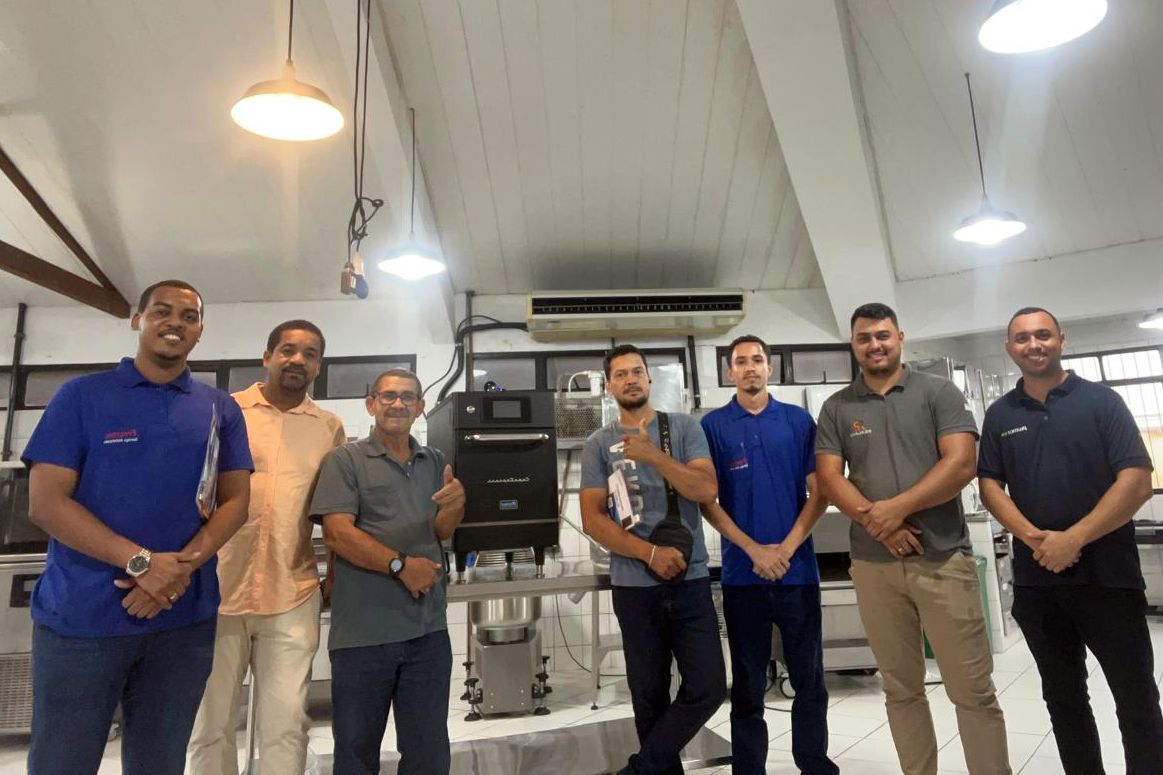 Grupo de homens em um laboratório, posando ao lado de equipamentos industriais sob luzes fortes.