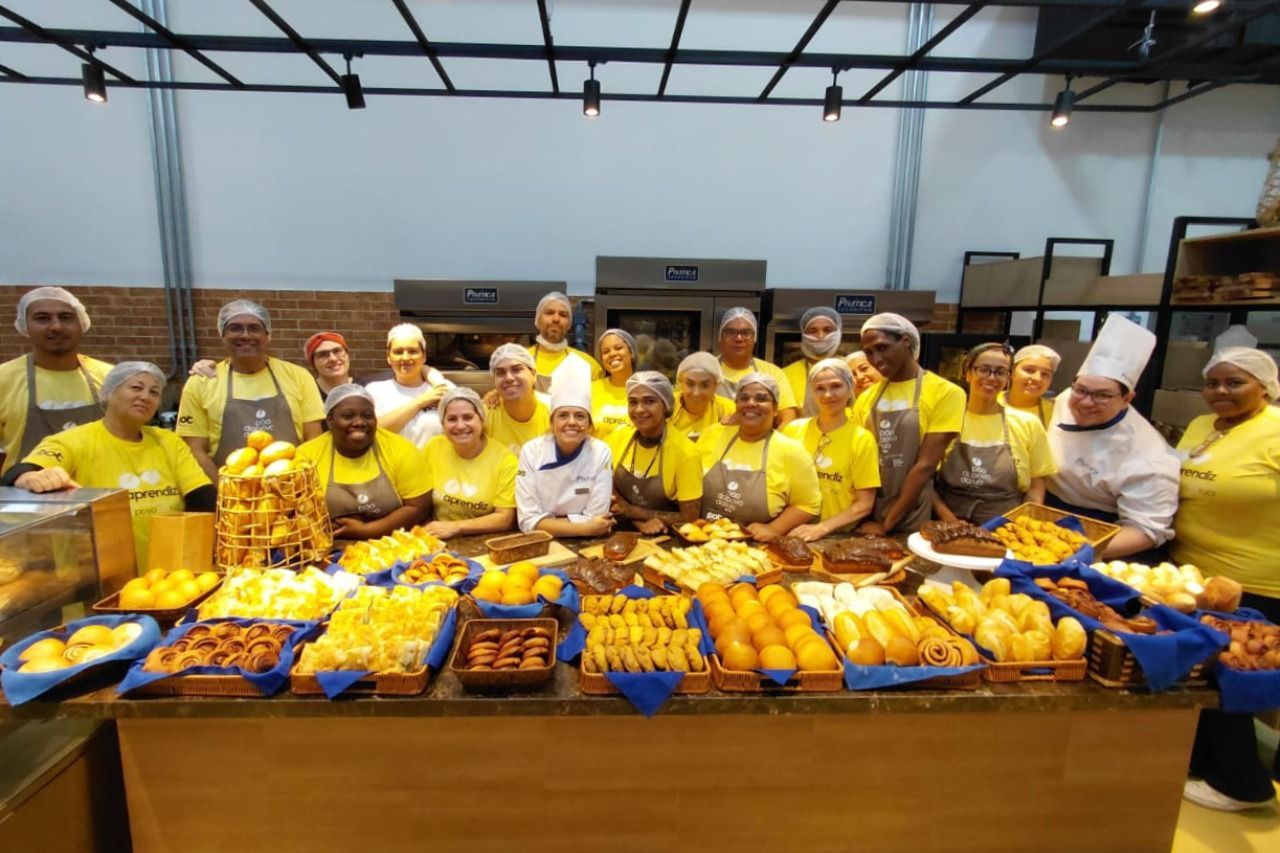 Um grupo de pessoas com camisas e aventais amarelos está atrás de um balcão de produtos de panificação.
