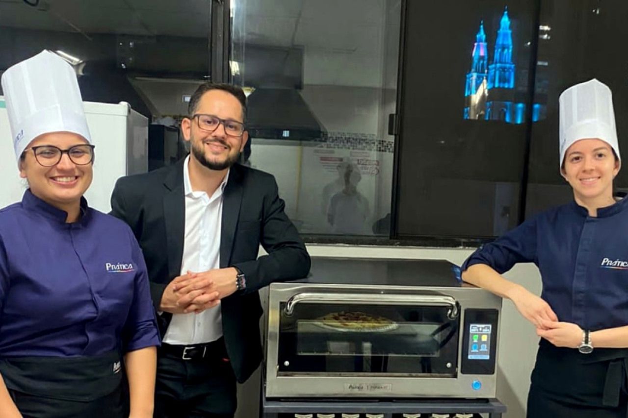 Um homem e duas mulheres estão de pé ao lado de um forno de pizza.
