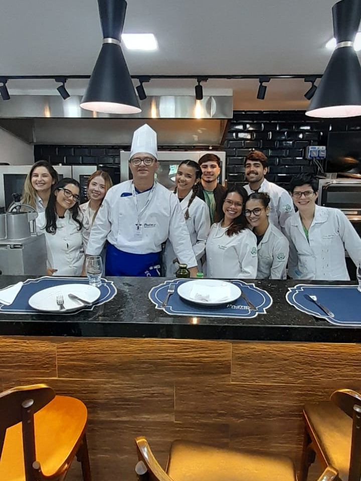 Chef e grupo de pessoas de jaleco branco sorrindo atrás de um balcão em um restaurante.