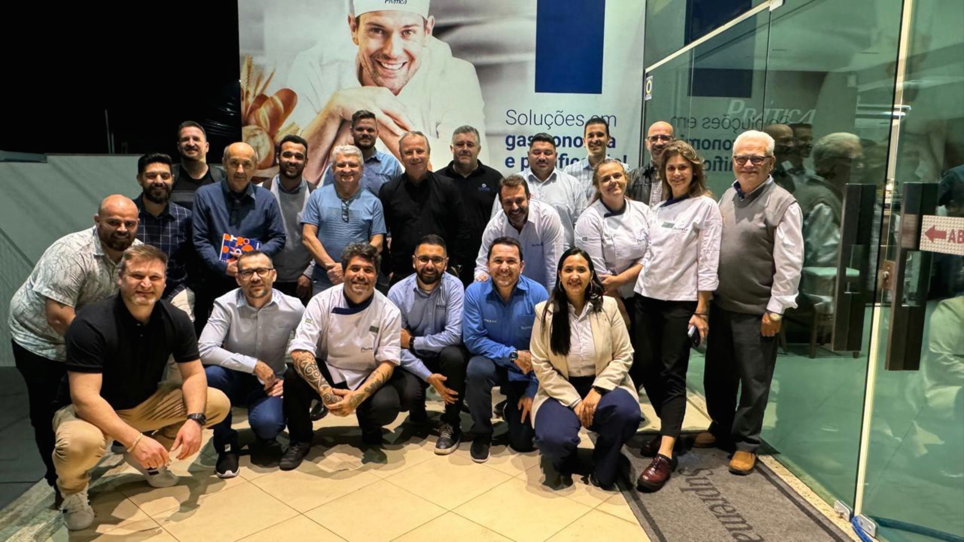 Um grupo de pessoas está posando para uma foto em frente a uma porta de vidro.
