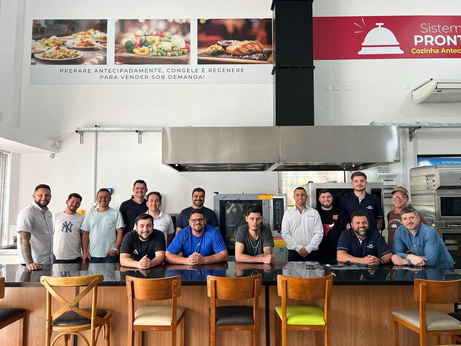 Grupo de pessoas em uma cozinha industrial, sorrindo, sob