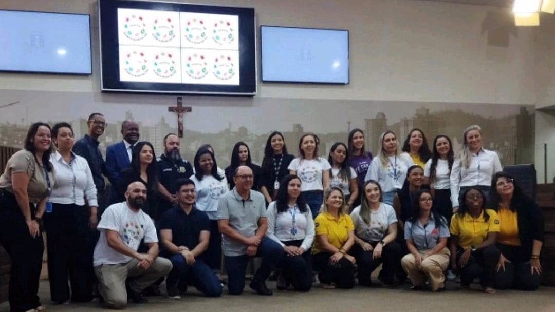 Um grupo de pessoas está posando para uma foto em frente a uma tela grande.