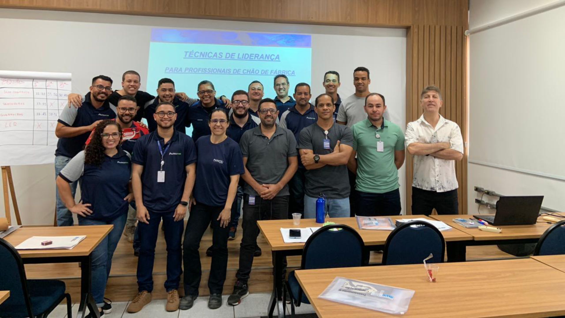 Um grupo de pessoas está posando para uma foto em uma sala de aula.