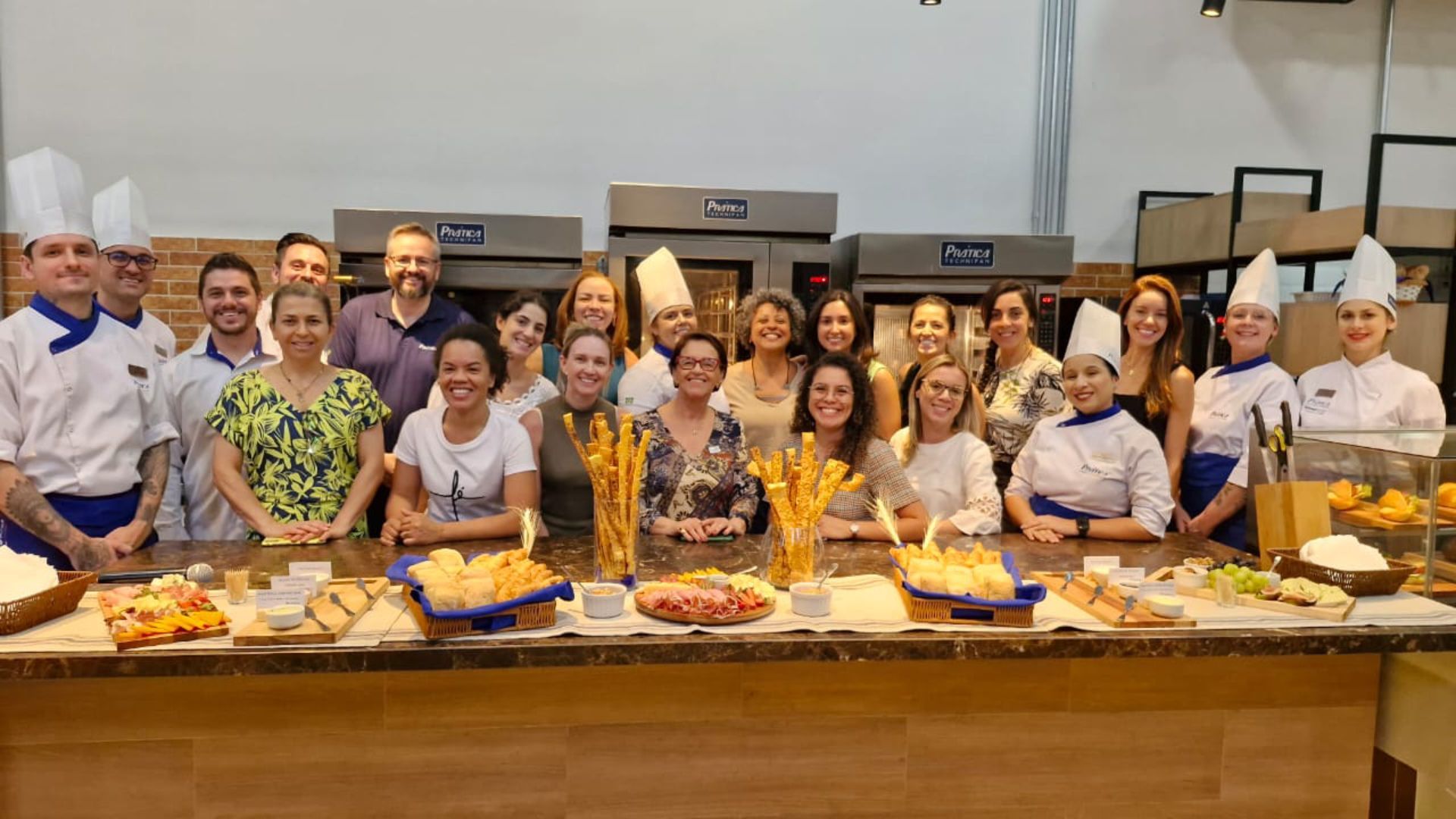 Um grupo de pessoas está posando para uma foto em frente a uma mesa cheia de comida.