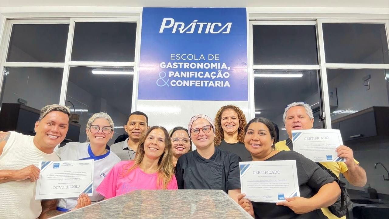 Grupo de pessoas com certificados em frente à placa de uma escola de culinária, sorrindo.