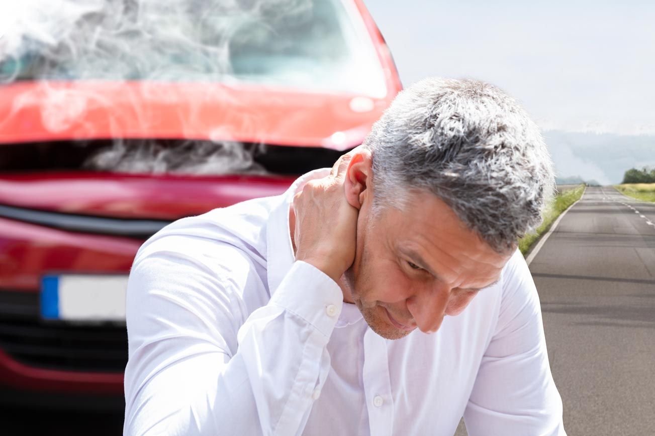 Man holding neck in pain near a damaged red car on a roadside in Eastover, NC.